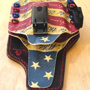 Pu&ograve; includere: Una fondina personalizzata con un design a bandiera americana. La fondina ha una combinazione di colori rosso, bianco e blu con testo e stelle. Include una clip nera e viti rosse e blu.