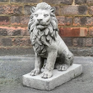 Può includere: Una scultura di pietra grigia di un leone seduto su una base quadrata. Il leone ha una criniera dettagliata e un'espressione realistica.