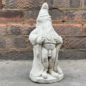 May include: A white concrete garden gnome statue wearing a robe and a pointed hat. The gnome is standing with its arms crossed and has a beard.