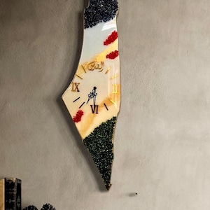 Op de afbeelding: Een klok in de vorm van de omtrek van Palestina met een witte wijzerplaat en gouden Romeinse cijfers. De klok is versierd met blauwe, groene en rode glitter. Het Arabische woord voor "Palestina" staat in goud op de wijzerplaat van de klok.