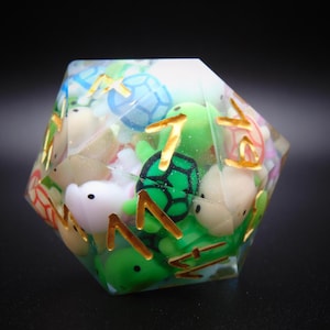 May include: A clear, multi-sided dice with a variety of small, colorful turtle and sea creature figurines inside. The dice is made of resin and has a gold-colored outline.
