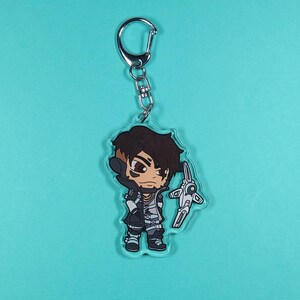 May include: A cartoon character keychain featuring a character with brown hair, a black and white outfit, and a white weapon. The keychain is made of clear acrylic.