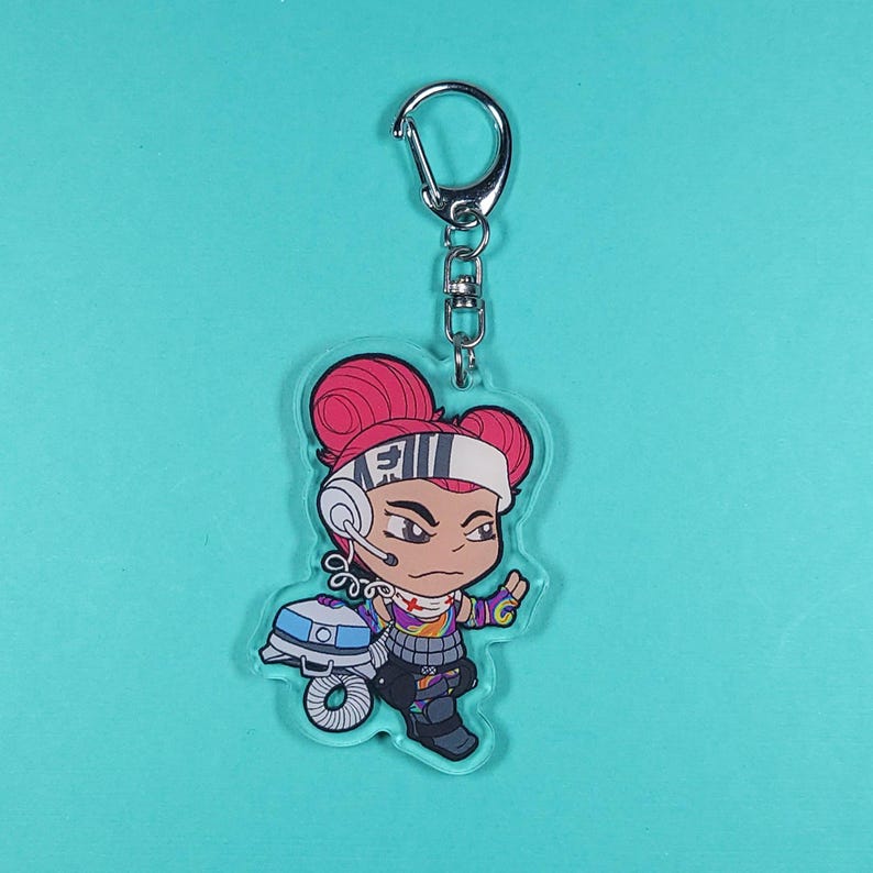 May include: A clear acrylic keychain featuring a cartoon character with red hair, a black and white headband, and a colourful outfit. The character is holding a small, round object with a blue and white design. The keychain is attached to a silver metal ring.