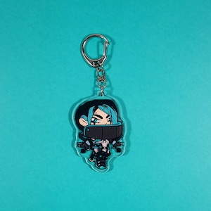 May include: A clear acrylic keychain featuring a cartoon character with blue hair, a black mask, and a blue and black outfit. The character is holding a gun in their right hand.