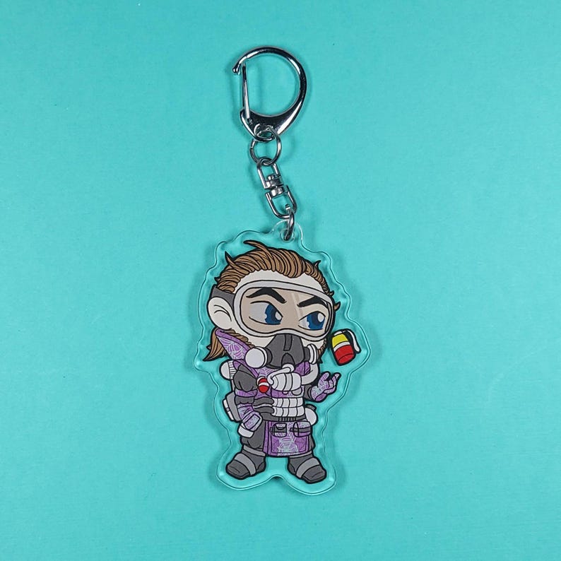 May include: A purple and white cartoon character with a gas mask and a yellow can in their hand. The character is attached to a silver keychain.