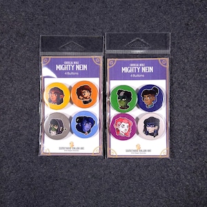 May include: Two sets of six 2.25 inch button pins featuring characters from the Critical Role animated series Mighty Nein. The buttons are packaged in clear plastic with a header card that reads "Critical Role Mighty Nein 4 Buttons" and "Something Major Art".