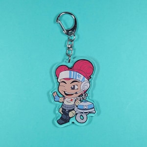 May include: A pink and white cartoon character with red hair and a headset, holding a white and blue robot. The character is on a clear acrylic keychain.
