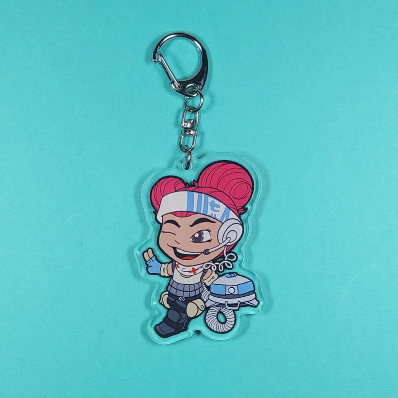 May include: A pink and white cartoon character with red hair and a headset, holding a white and blue robot. The character is on a clear acrylic keychain.