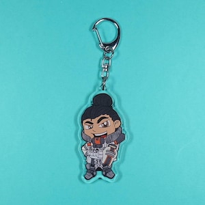 May include: A clear acrylic keychain featuring a cartoon character with brown hair, a white and orange outfit, and a black and white gun. The character is smiling and has a determined expression.