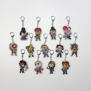 May include: A set of 12 colourful character keychains featuring characters from the video game Apex Legends. The keychains are made of clear acrylic and feature a variety of characters, including Bloodhound, Lifeline, and Mirage.