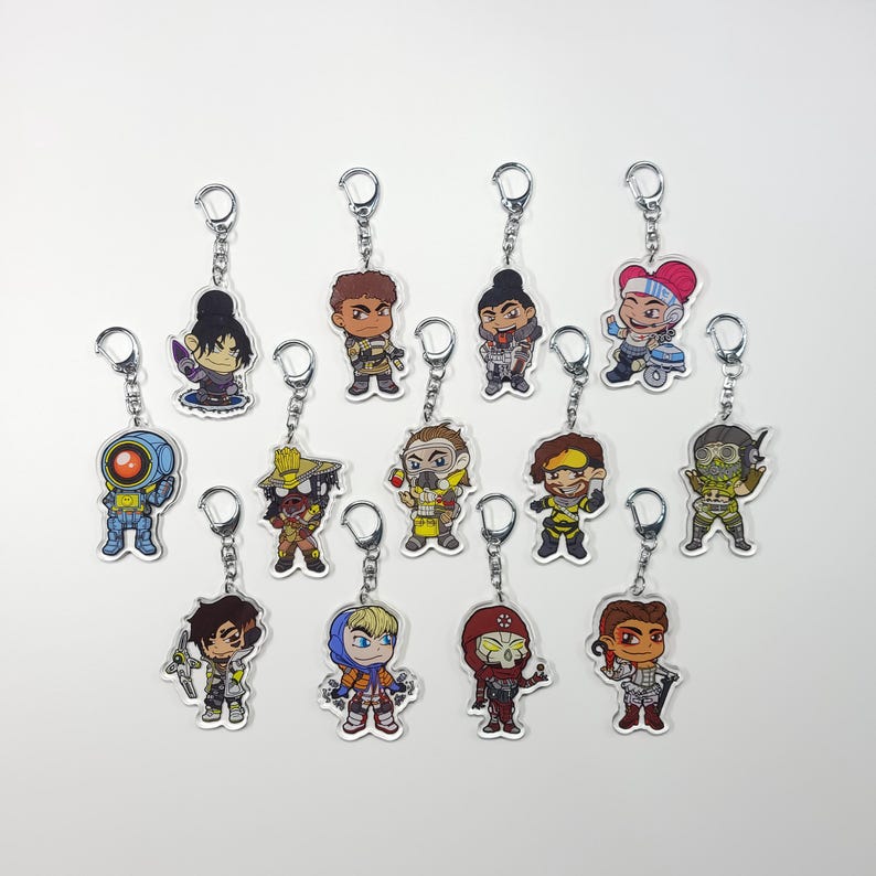 May include: A set of 13 colourful character keychains featuring characters from the video game Apex Legends. The keychains are made of clear acrylic and feature a variety of characters, including Bloodhound, Lifeline, and Mirage.