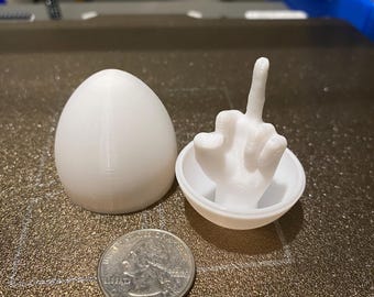 May include: White 3D printed egg-shaped container with a white 3D printed hand giving the middle finger inside.