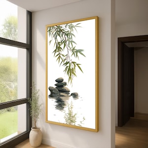 May include: A framed artwork featuring a zen-inspired scene. The image depicts a stack of gray stones in water, with green bamboo leaves hanging from above. The artwork is encased in a gold frame and hangs on a white wall.