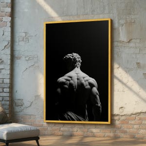 May include: A black and white framed print of a classical sculpture depicting a muscular male figure from the back. The artwork is set against a dark background, with a gold frame. The image is mounted on a textured wall.