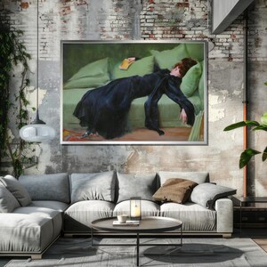 May include: A painting of a woman in a black dress lying on a green couch. She is holding a book in her hand and her head is resting on a pillow. The painting is framed in a silver frame.