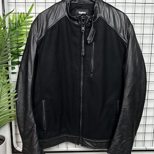 Könnte beinhalten: Eine schwarze Leder- und Wolljacke mit Reißverschluss und dem Wort "tigha" auf dem Etikett.