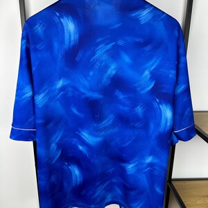 May include: A blue short-sleeved shirt with a white trim and an abstract blue and white paint-splatter design.