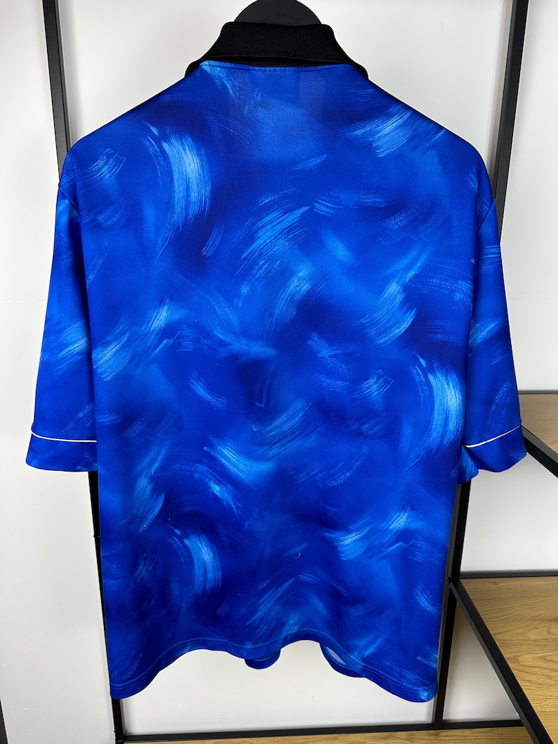 May include: A blue short-sleeved shirt with a white trim and an abstract blue and white paint-splatter design.