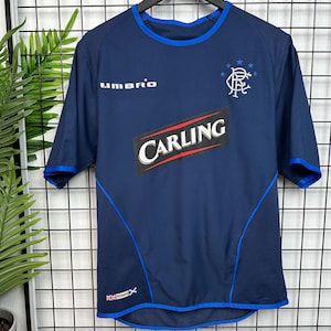 May include: A navy blue soccer jersey with a white "UMBRO" logo on the left chest, a white "CARLING" logo on the front, and a white Rangers FC crest with stars on the right chest.