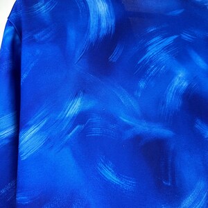 May include: A blue shirt with a white abstract brushstroke pattern.