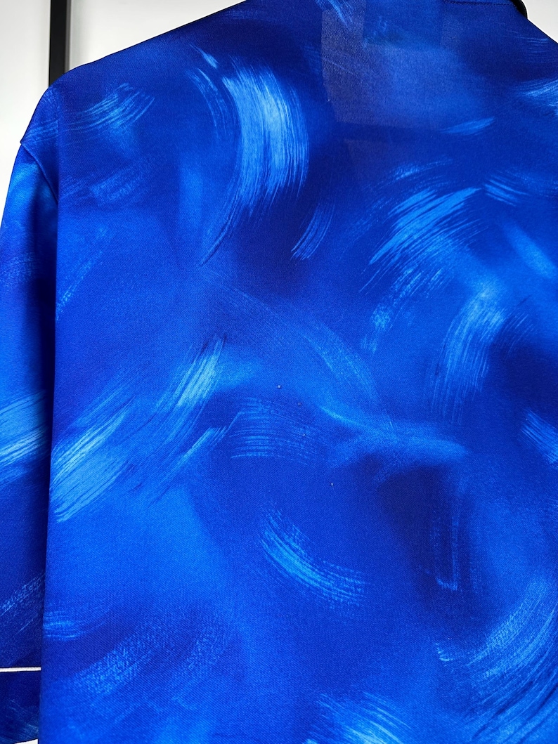 May include: A blue shirt with a white abstract brushstroke pattern.
