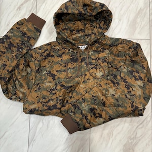 以下が含まれることがあります： 茶色、緑、黒の色合いのカモフラージュ柄のクロップド丈フード付きジャケット。 ジャケットは、ドローストリングフード、フロントジッパー、茶色のリブ編みカフスが特徴です。 ジャケットはキルティング素材で作られています。