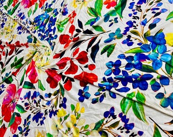 May include: White fabric with a colourful floral print. The print features red, blue, yellow, and green flowers on a white background.