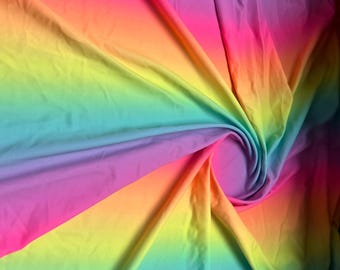 May include: A smooth fabric featuring a vibrant rainbow gradient pattern that transitions through shades of pink, purple, blue, green, yellow, and orange. The material is gathered into a central swirl, creating soft folds and shadows.