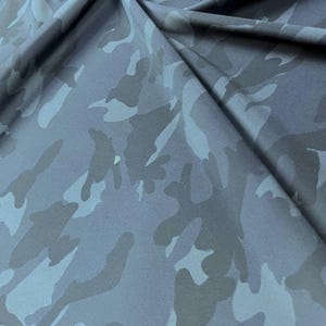 Puede incluir: Primer plano de una tela con un patrón de camuflaje. La tela presenta tonos de azul y gris en un diseño repetitivo. La tela está doblada, mostrando la textura y la caída del material.