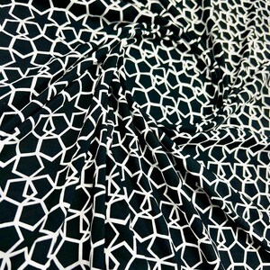 May include: Black fabric with a repeating white star and geometric pattern. The fabric is draped, creating folds and shadows that highlight the design. The star shapes are outlined in white against the dark background.