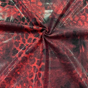 May include: Red fabric with a black and silver leopard print pattern. The fabric has a shiny, metallic finish.