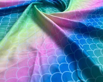 May include: A vibrant fabric with a mermaid scale pattern. The material features a gradient of colors, including blue, green, yellow, pink, and purple. The scales are white and create a textured effect across the surface.