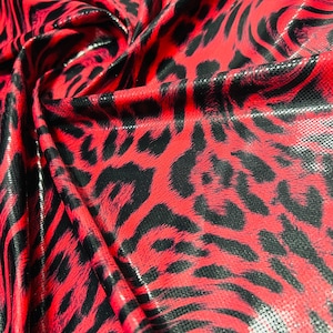 Puede incluir: Tela con estampado de animales en rojo y negro con una superficie brillante. La tela presenta un patrón audaz de manchas y rayas negras sobre un fondo rojo vibrante. El material está doblado, mostrando su textura y brillo.