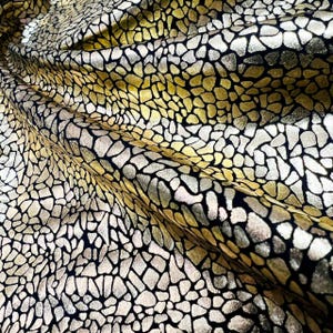 Op de afbeelding: Zwarte stof met een gouden en zilveren mozaïekpatroon. De stof is textuur en heeft een metallic glans.