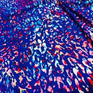 Puede incluir: Una tela con un vibrante estampado animal sobre una base de color azul intenso. El diseño se compone de formas irregulares e interconectadas en tonos rosa brillante, azul claro y blanco, creando una textura multicolor de alto contraste.