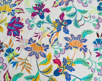 May include: White fabric with a colourful floral design. The pattern showcases large, stylised flowers in blue, orange, pink, and yellow, with green leaves and stems. The style is reminiscent of a botanical illustration.