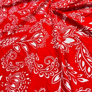 May include: Red fabric with a white paisley pattern. The fabric is soft and has a smooth texture.