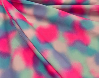May include: A close-up of a pink, blue, and green tie-dye fabric. The fabric has a soft, flowing texture and is perfect for crafting projects.