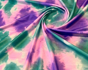 May include: A colourful fabric with a tie-dye design in pink, purple, and teal. The material is gathered and folded, producing a swirling effect. The colours blend, creating a soft, watercolour-like appearance.