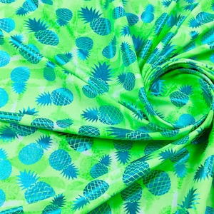 Puede incluir: Tela verde con un patrón repetido de piñas azules. Las piñas están delineadas en un azul más oscuro y tienen un acabado brillante y metálico.