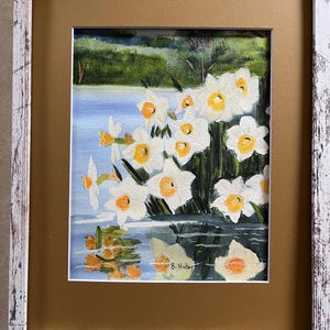May include: Watercolor painting of white and yellow daffodils by a body of water, framed in a white distressed wood frame with a gold mat. The painting includes reflections of the flowers in the water. Signed "B. Huber".