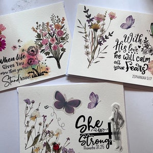 May include: Three handmade greeting cards with floral and butterfly designs. One card features the text "When life gives you more than you can stand, kneel." Another card has the text "With His love he will calm all your fears." The third card says "She is strong."