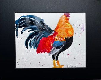 May include: A colorful painting of a rooster, featuring a vibrant orange body, red and blue accents, and a black tail. The artwork is set against a white background with pink paint splatters and is framed in a black mat.