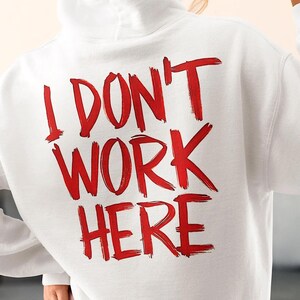 May include: White hooded sweatshirt with the phrase "I DON'T WORK HERE" printed in red on the back.
