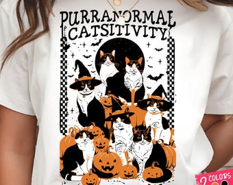 Könnte beinhalten: Weißes T-Shirt mit einem Halloween-Motiv. Das Design zeigt schwarz-weiße Katzen mit Hexenhüten, Kürbissen und dem Text "PURRANORMAL CATSITIVITY". Fledermäuse und Sterne sind ebenfalls im Bild enthalten.