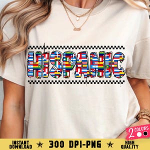May include: A cream-coloured t-shirt displays the word "HISPANIC" in large, colourful letters. Each letter is filled with a flag design, and the word is outlined with a black and white chequered pattern. The shirt has short sleeves.
