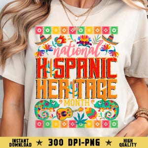 May include: A cream-colored t-shirt featuring a vibrant design celebrating National Hispanic Heritage Month. The design includes the text "National Hispanic Heritage Month" in bold, colorful letters, along with images of sombreros, chameleons, and a guitar.