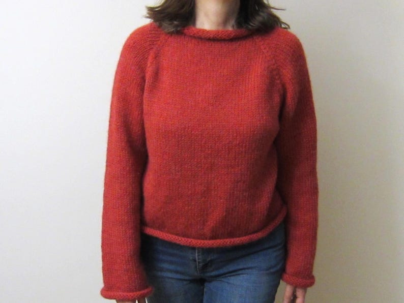 Puede incluir: Un su&eacute;ter de punto color &oacute;xido con cuello redondo y mangas largas. El su&eacute;ter tiene un dobladillo y pu&ntilde;os acanalados. La modelo lleva vaqueros azules. El su&eacute;ter est&aacute; hecho de un material suave y texturizado.