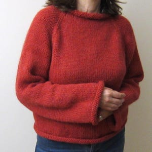 Puede incluir: Un su&eacute;ter rojo tejido con un cuello ancho y mangas largas. El su&eacute;ter tiene un dobladillo y pu&ntilde;os acanalados. Las mangas son de estilo ragl&aacute;n. El su&eacute;ter est&aacute; hecho de un hilo grueso y texturizado.