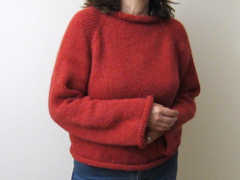 Puede incluir: Un su&eacute;ter rojo tejido con un cuello ancho y mangas largas. El su&eacute;ter tiene un dobladillo y pu&ntilde;os acanalados. Las mangas son de estilo ragl&aacute;n. El su&eacute;ter est&aacute; hecho de un hilo grueso y texturizado.